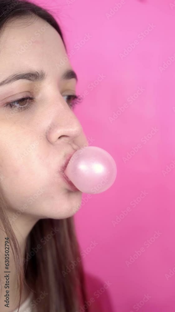 Young brunette woman making bubblegum baloons on pink background