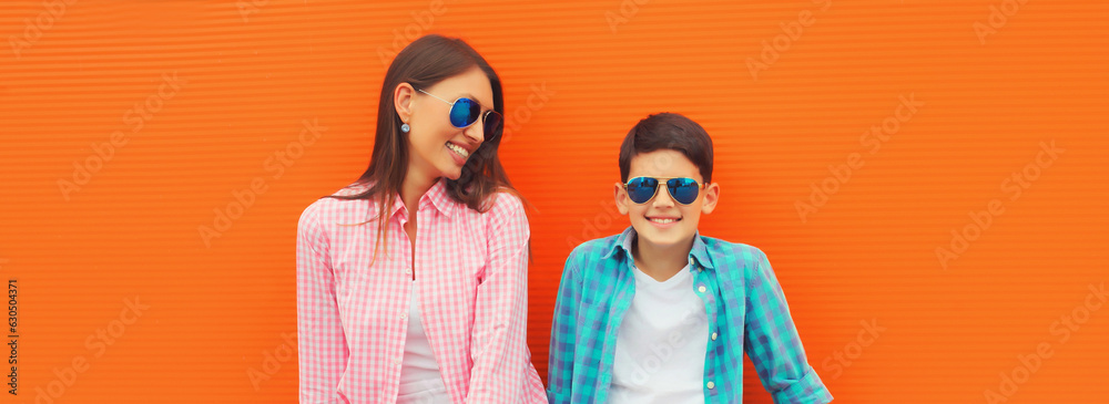 Stylish happy smiling mother with son teenager posing together in sunglasses, checkered shirts, jeans in the city on orange background Stylish happy smiling mother with son teenager posing together in sunglasses, checkered shirts, jeans in the city on orange background