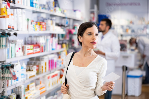 Woman chooses medical products in pharmacy, checking the list on a piece of paper