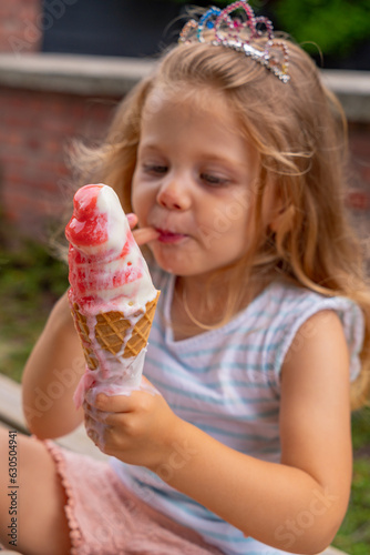 Cute little girl eating ice cream in the summer garden. Selective focus.