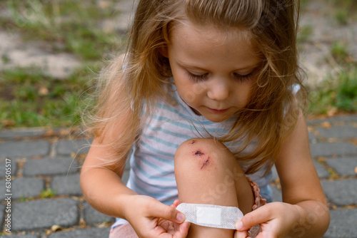 A little girl accident and plaster with a band aid on the knee of boy with an injury, wound or pain. Kids, cut and heal with the hands of a male child outside with a scrape