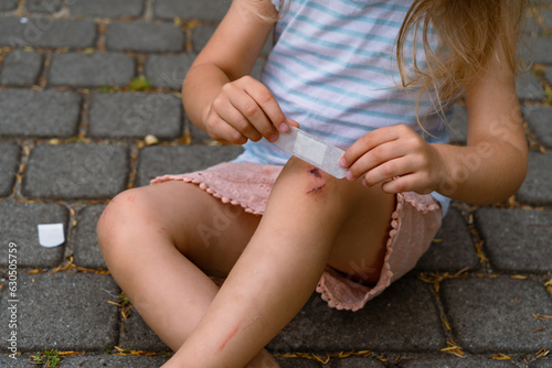 A little girl puts a band-aid on a wound on her knee after an accident. Selective focus.