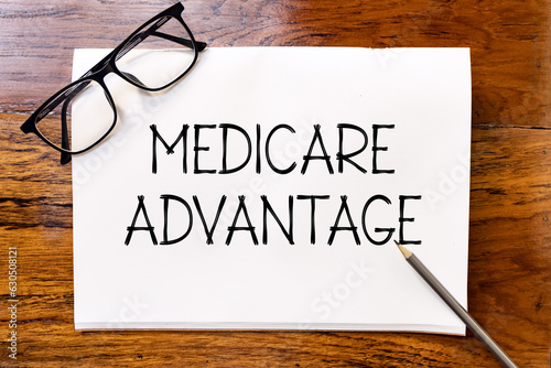 Obraz na plátně Medicare advantage handwriting text on blank notebook paper on wooden table with pencil and glasses aside