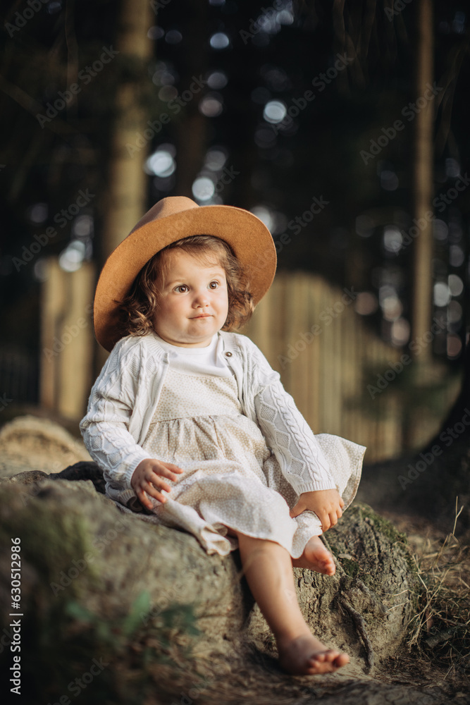 Obraz premium Little girl wearing hat, sitting bootless in the countryside