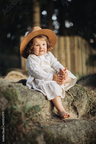 Fototapeta Naklejka Na Ścianę i Meble -  Little girl wearing hat, sitting bootless in the countryside