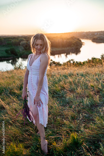 Pretty slim young woman with wildflowers on nature background in summer at sunset full-length. female is relaxing in the field with flowers. 
