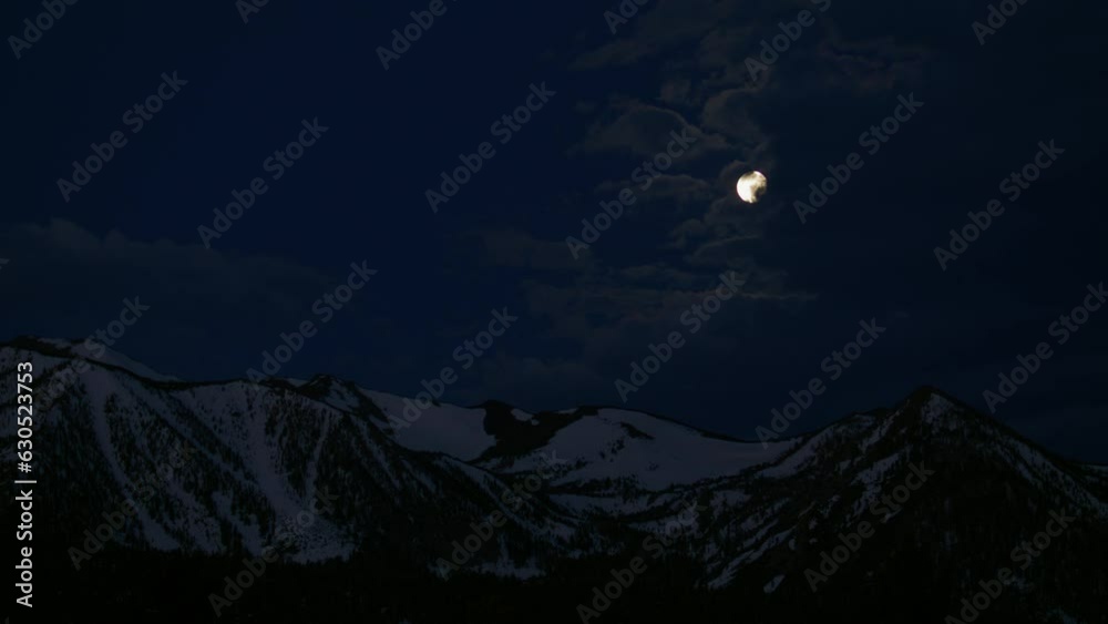 Clouds moving past full moon in night sky with snowcapped mountains underneath Clouds moving past full moon in night sky with snowcapped mountains underneath