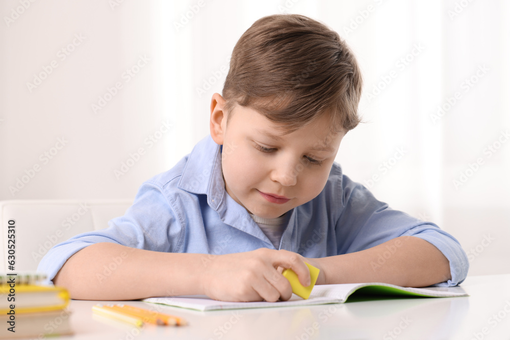 Little boy erasing mistake in his notebook at white desk indoors Little boy erasing mistake in his notebook at white desk indoors