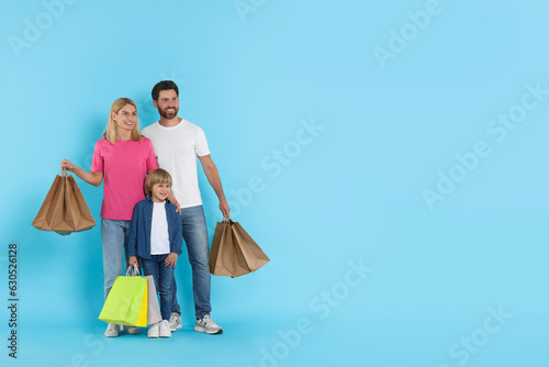 Happy family with shopping bags on light blue background. Space for text