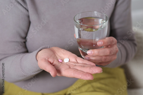 Senior woman with glass of water and pills indoors, closeup