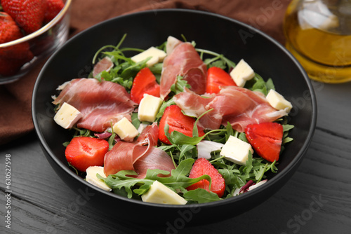 Tasty salad with brie cheese, prosciutto and strawberries on grey wooden table, closeup