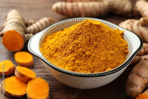 Bowl with aromatic turmeric powder and cut roots on wooden table, closeup