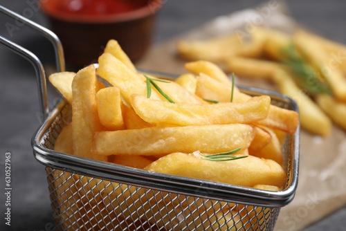 Metal basket with tasty French fries and rosemary on table, closeup