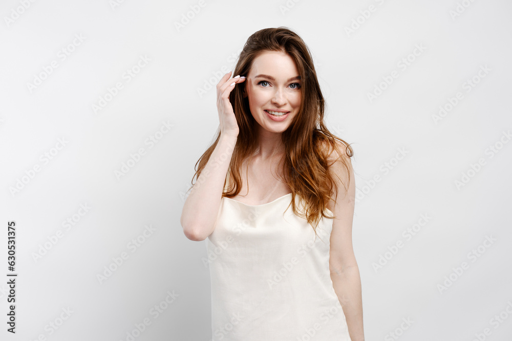 Smiling sexy woman in nightgown fixing hair, looking at camera posing isolated on gray background