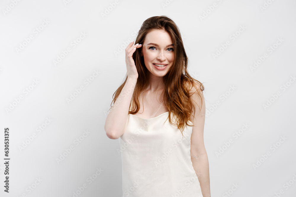 Smiling sexy woman in nightgown fixing hair, looking at camera posing isolated on gray background Smiling sexy woman in nightgown fixing hair, looking at camera posing isolated on gray background