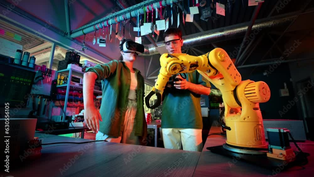 Teens doing experiments in robotics in a laboratory. Boy in protective glasses and girl in VR headset controlling the robot using controller and hand. Red and blue illumination
