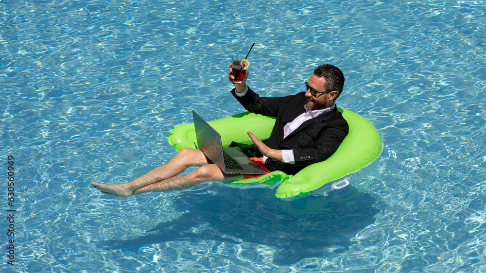 Summer vacations and freedom travel concept. Portrait of funny business man on the beach. Businessman in suit floating with laptop and cocktail in pool. Crazy business man dreams on summer vacation.