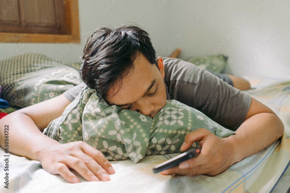Portrait of Asian man fall asleep while holding smartphone laying down on bed Portrait of Asian man fall asleep while holding smartphone laying down on bed
