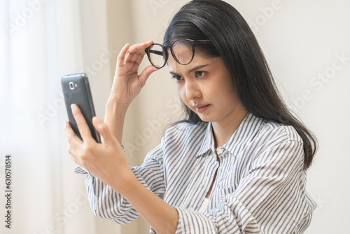 Presbyopia, Hyperopia middle aged asian woman holding eyeglasses problem with vision blurred ,trying to read text message from smart mobile phone screen, eye disease of old, eyesight farsightedness. photo