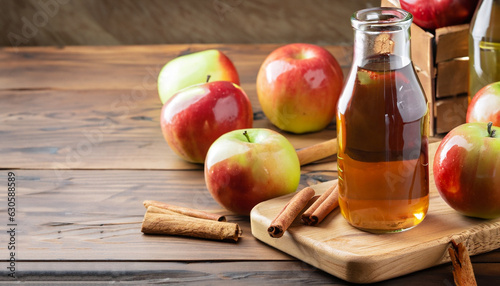 Apple cider in glass bottle with cinnamon sticks and fresh apples on cutting board, on wooden background
