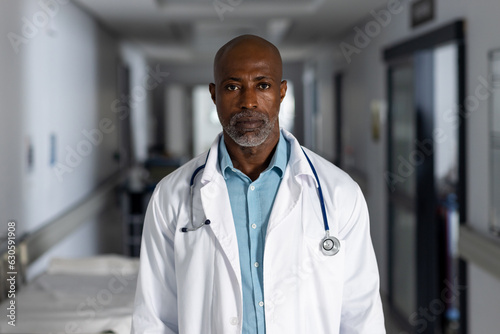 Portrait of african american male doctor wearing lab coat in corridor at hospital
