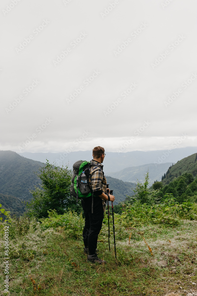 Portrait of a man in the mountains: he stands with a backpack on his back, in front of him, a view of a misty valley unfolds.