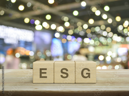 ESG letter on wood block cubes on wooden table over blur light and shadow of shopping mall, Environmental Social Corporate Governance concept © grapestock