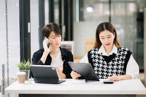 Asian business colleague business presents and explains and using laptop and tablet. Teamwork, financial marketing team, while sitting in modern office room..