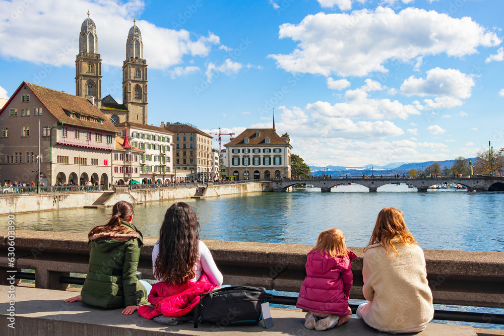 Panoramic view of the Limmat River in Zurich, Monterbrücke Cathedral Bridge and historic buildings and monasteries on the side. A group of girls sit and contemplate a fascinating cityscape.