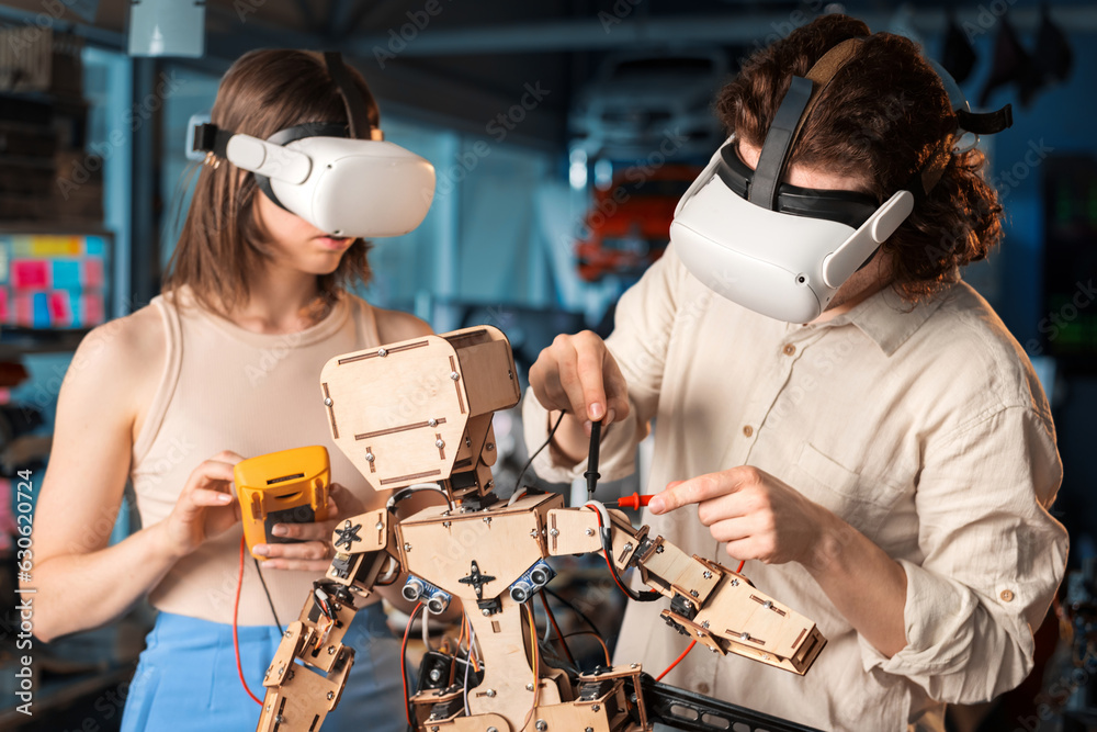 Young man and woman in VR glasses doing experiments in robotics in a laboratory