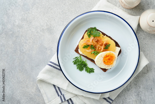 Open sandwich or smorrebrod with rye bread, herring, eggs, caramelized onions, parsley and cottage cheese on old wooden rustic table backgrounds. Danish or Scandinavian traditional food snack lunch.