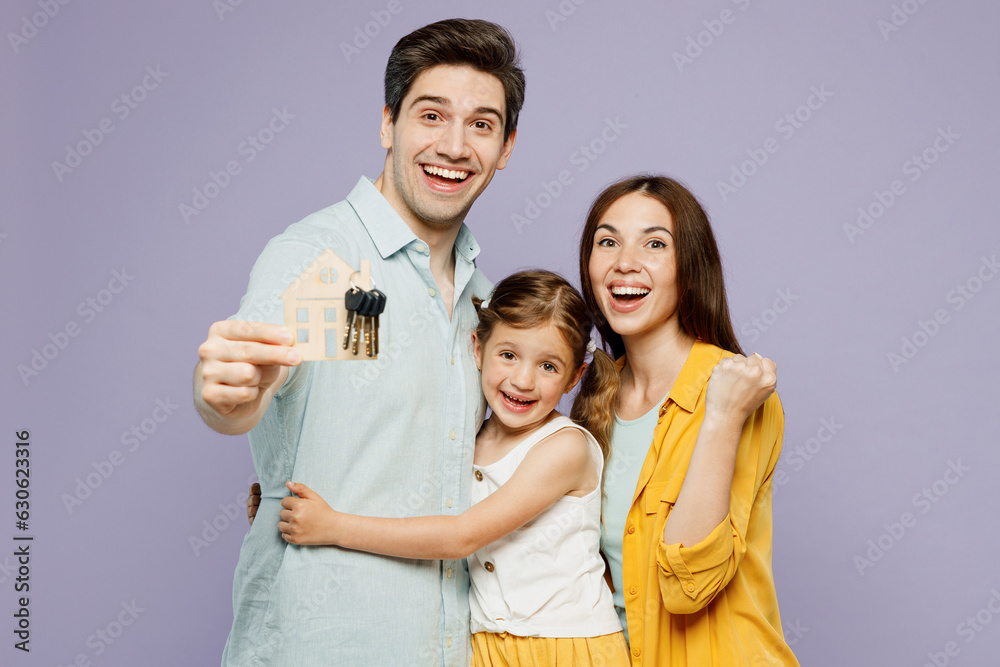 Young smiling happy parents mom dad with child kid daughter girl 6 years old wearing blue yellow casual clothes hold keys mock up of house, hug isolated on plain purple background. Family day concept. Young smiling happy parents mom dad with child kid daughter girl 6 years old wearing blue yellow casual clothes hold keys mock up of house, hug isolated on plain purple background. Family day concept.