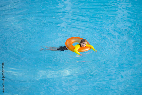 Swimming, summer vacation. Cute child playing in blue water. Kid enjoying summer vacation in water in the swimming pool. Cute little kid in swimming suit relaxing on an inflatable ring. Kid floating