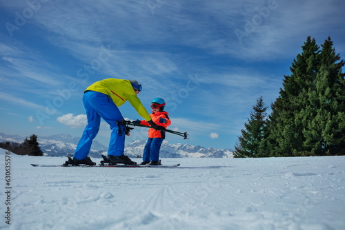 Dad show child how to ski going downhill holding poles in hands
