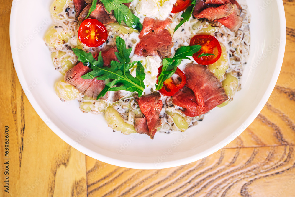 meat potato salad with tomatoes and pieces of beef on a plate in a cafe. light summer salad with potatoes and meat from a coffee house meat potato salad with tomatoes and pieces of beef on a plate in a cafe. light summer salad with potatoes and meat from a coffee house