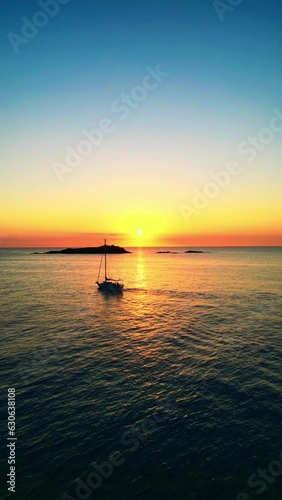 Reflejo de la salida del sol en el océano con isla y barco velero, DJI, toma lineal