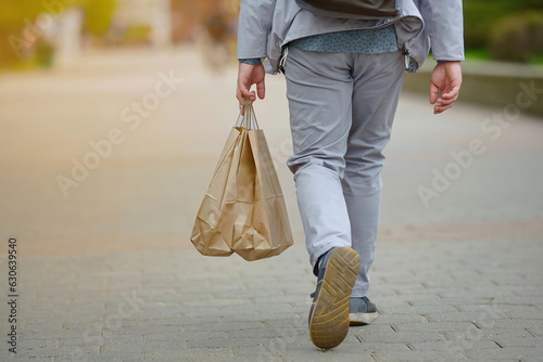 Man holding paper shopping bag walking down the street, rear view. Man shopaholic walking alone. photo