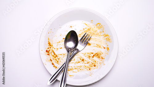Cutlery sits on a white plate of finished food on a white table.