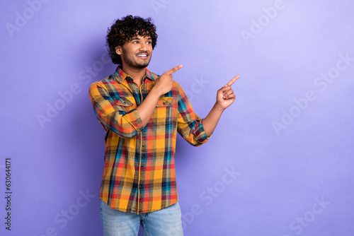 Photo of young man promoter student wear plaid shirt indicate fingers empty space looking advertisement isolated on purple color background