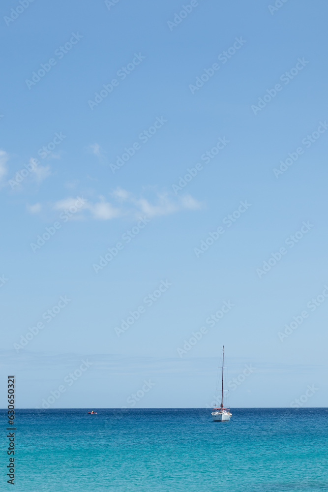 Seascape. Turquoise blue sea with sailboat in the background, sky with white clouds. Fuerteventura, Canary Islands, Spain 