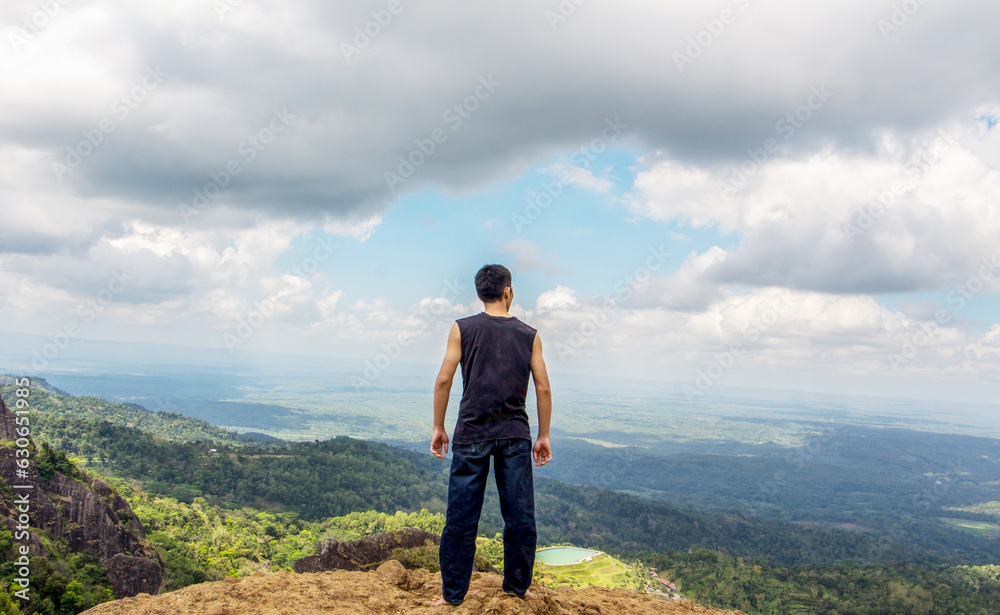 a man is in the middle of a view from the top of a hill with a stretch of blue sky and white clouds.