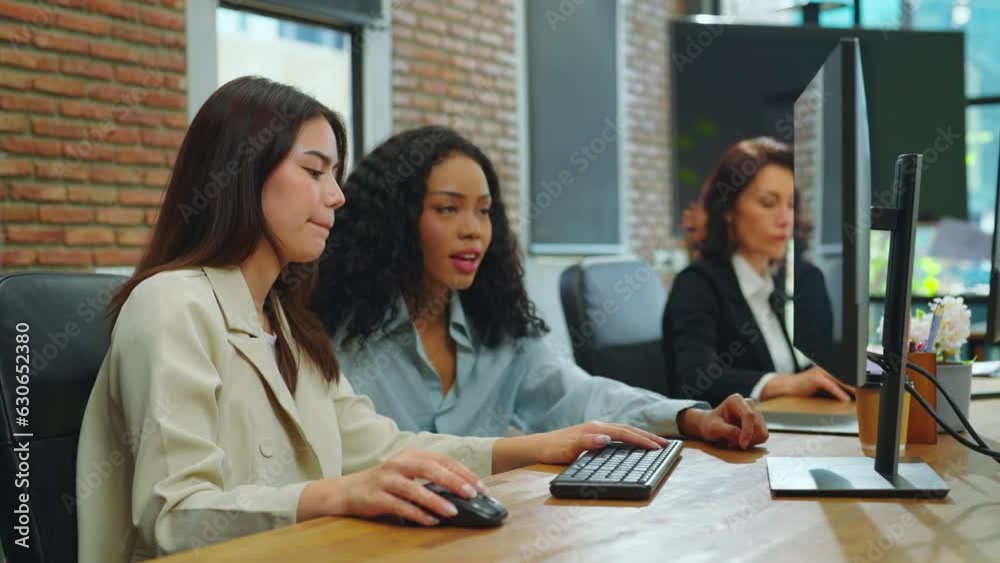 Two young women use computers to work at the office. They discuss projects together in the office. Two young women use computers to work at the office. They discuss projects together in the office.