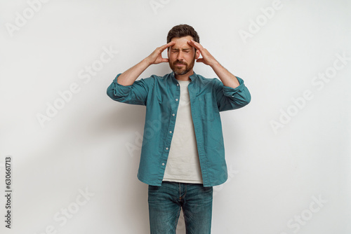 Man feeling sick, touching head and grimacing from painful headache standing on white background