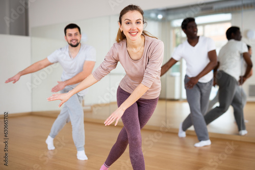 Energetic sporty young woman practicing modern vigorous dance movements in group dance class ..