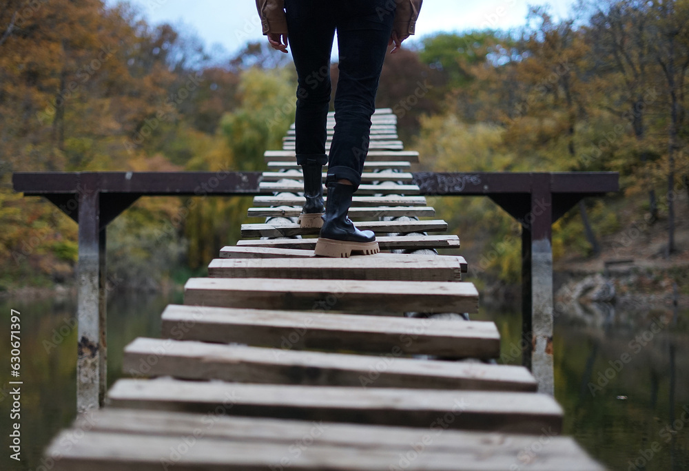 A girl in jeans and boots climbs up the wooden stairs above the forest lake