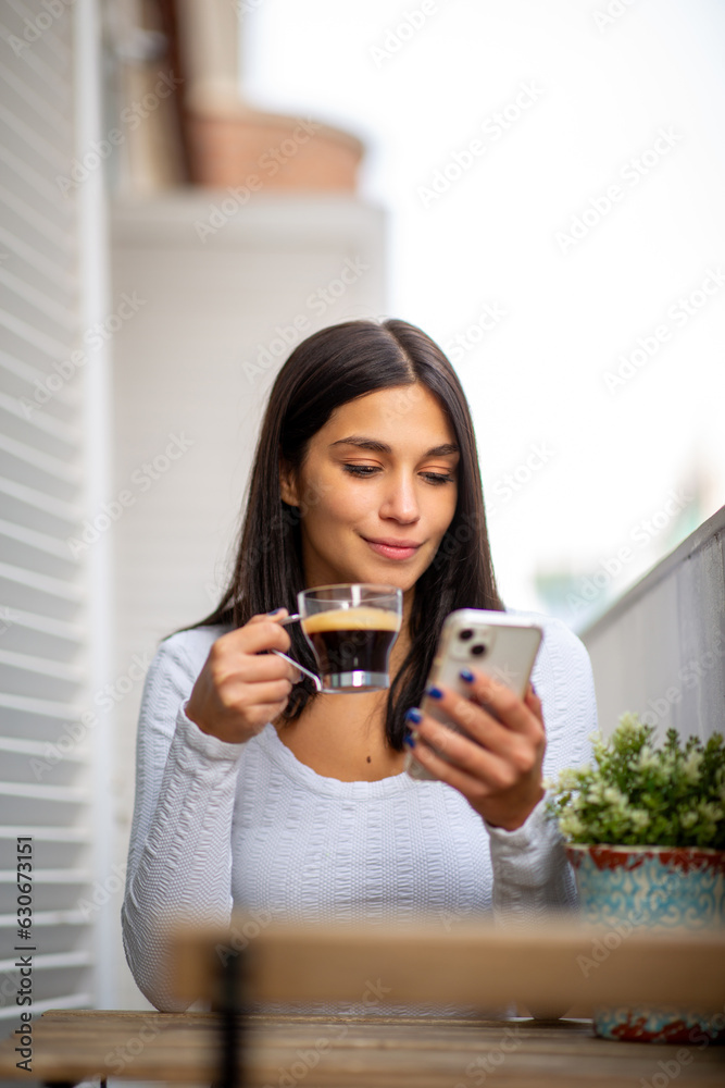woman sitting on balcony with mobile phone and cup of coffee in hand woman sitting on balcony with mobile phone and cup of coffee in hand