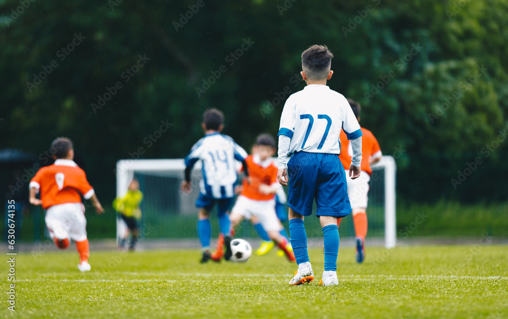 Obraz premium Young school boys playing soccer game. European soccer match between youth teams. Junior competition between players running and kicking a soccer ball. Tournament game between red and blue kids' teams