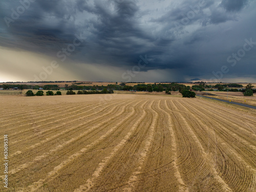 Aerial view of harvester lines in a dry paddock under rain falling from a dark stormy sky photo