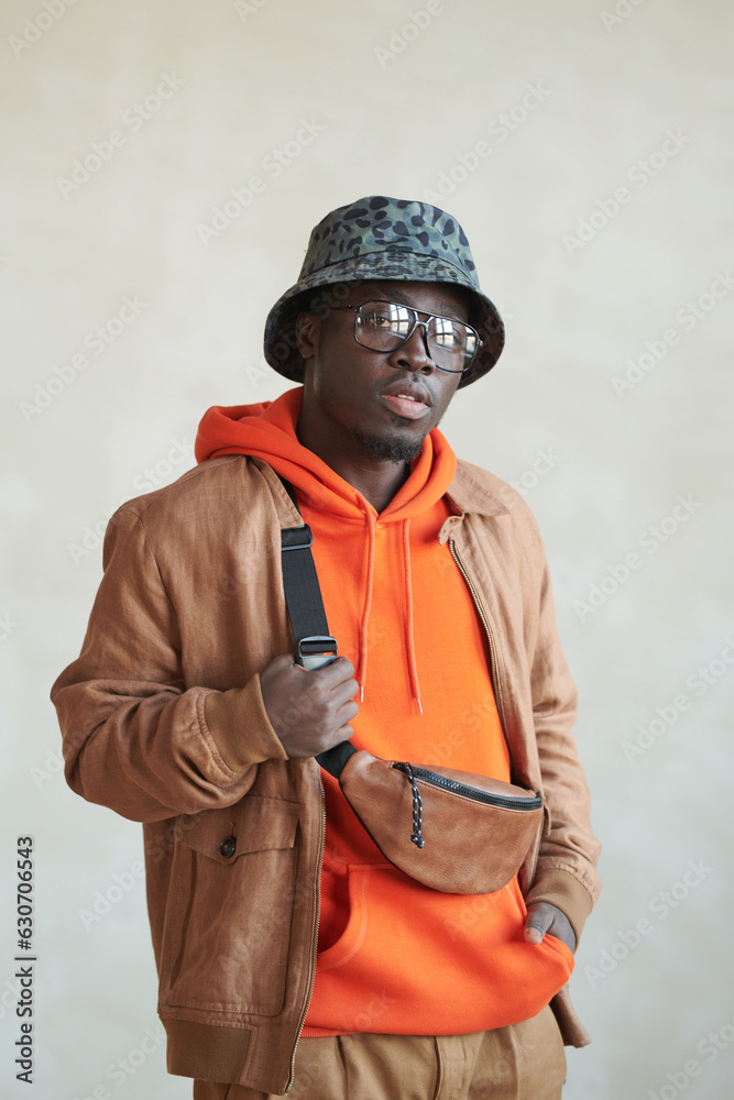 Obraz premium Medium studio portrait shot of handsome young Black man wearing stylish casual hoodie, jacket, bucket hat and belt bag looking at camera