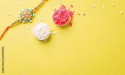 Raksha Bandhan, Indian festival with beautiful Rakhi and Rice Grains on yellow background. A traditional Indian wrist band which is a symbol of love between Sisters and Brothers